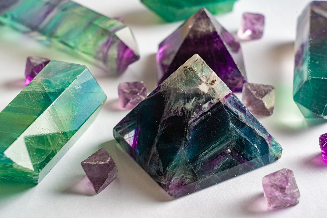 Close-up of colorful fluorite and amethyst crystals in various shapes on a white surface.